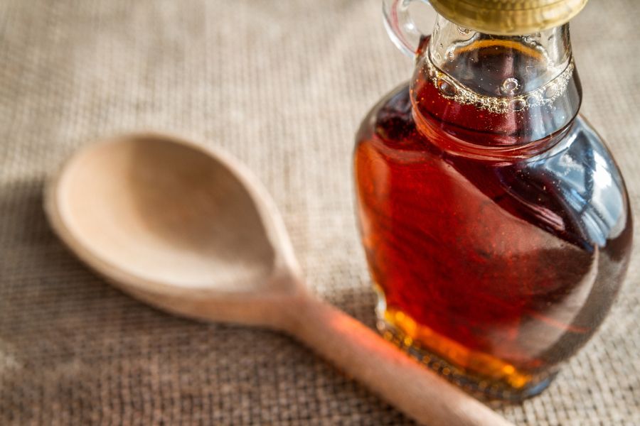 Jar of maple syrup beside a spoon